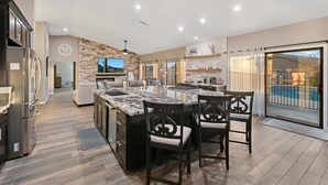 A modern kitchen with a large island, dark cabinetry, and a stone accent wall. - Luxury Home, Beautiful Neighborhood, Spacious for Family, with Pool/Spa.  (Glendale)