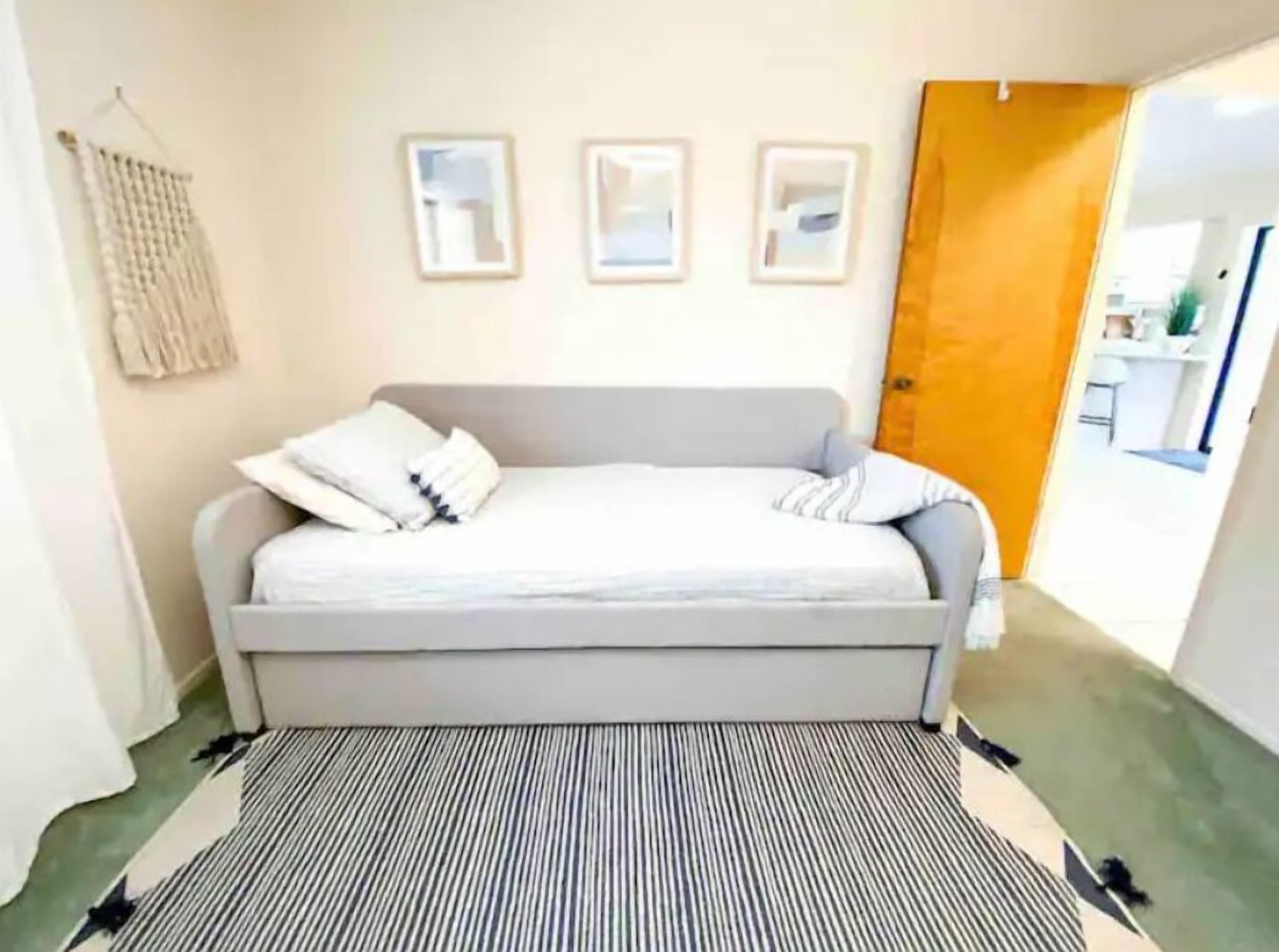 Une chambre avec un canapé-lit gris, un tapis à rayures et trois tableaux encadrés accrochés au mur.