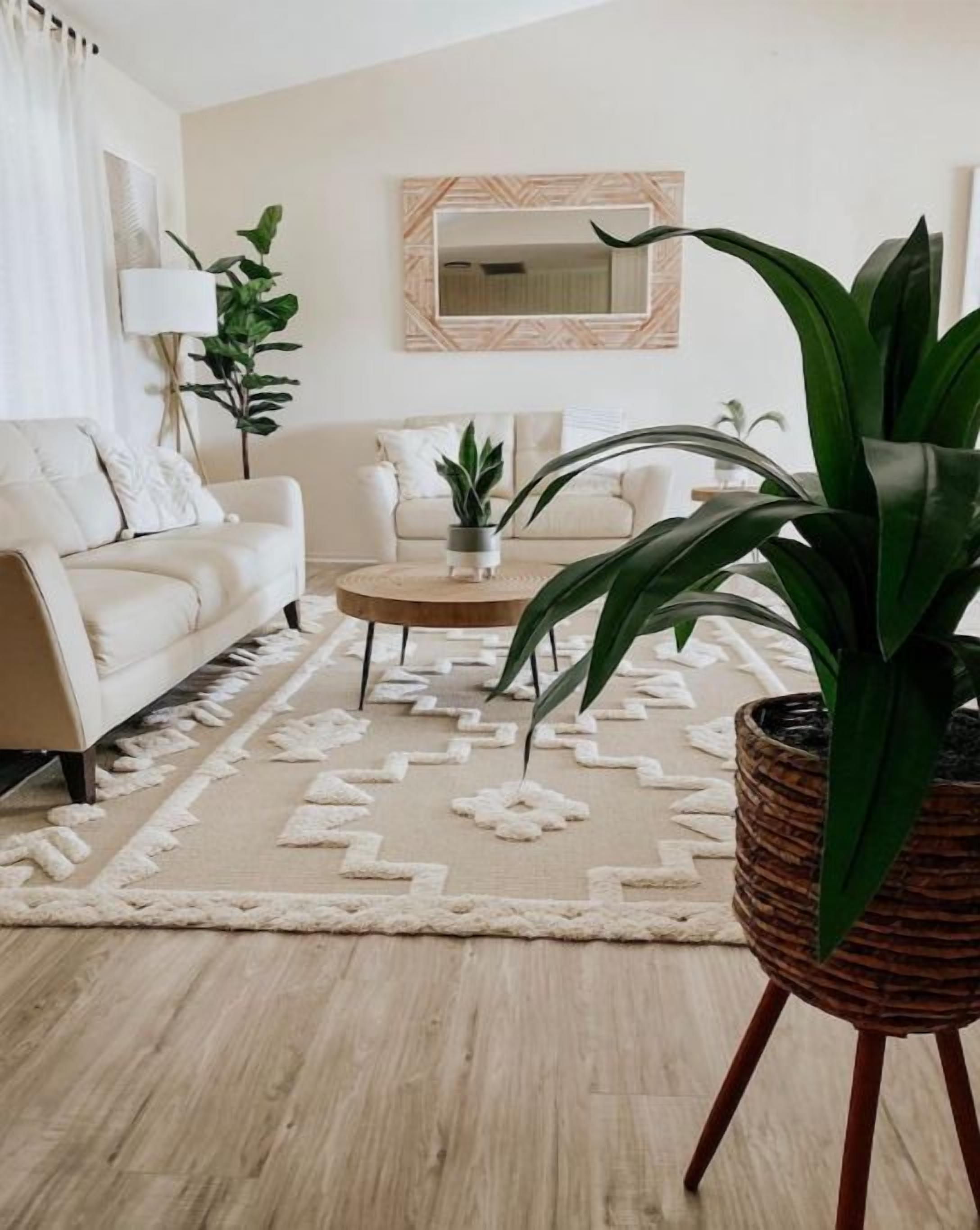 Ein Wohnzimmer mit einem beigefarbenen Sofa, einem Couchtisch und einer großen Küstpflanze.