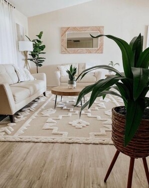 Una sala de estar con un sofá color crema, una mesa de centro y una planta grande en maceta.