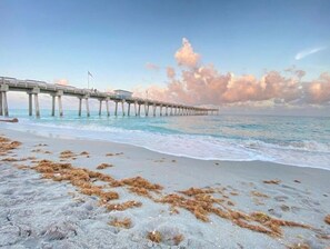 A beach with a pier extending into the ocean, featuring a flag on top.