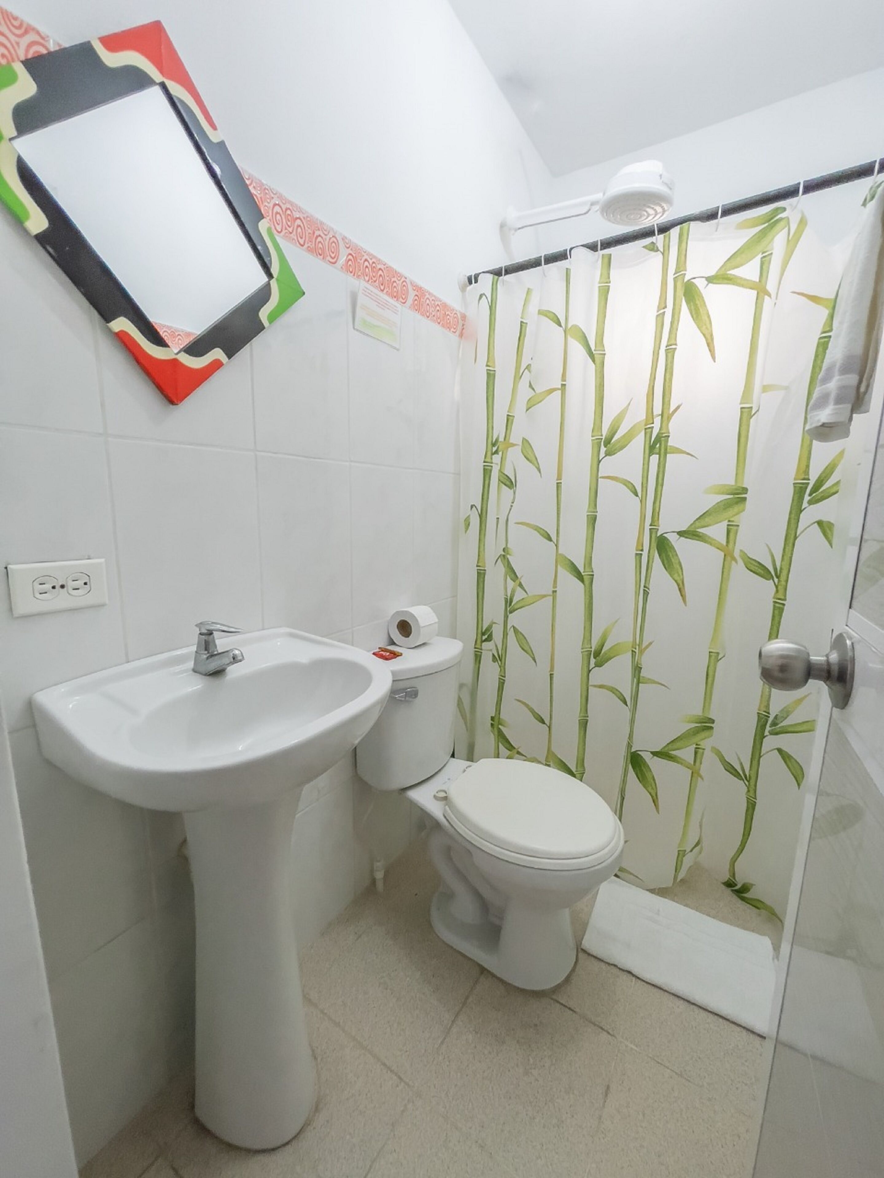 Et badeværelse med et konsolbordvask, toilet og en bruseniche med bambusbrusevæg.