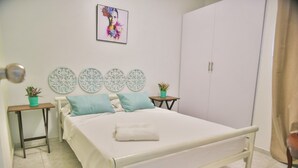 Een keurig opgemaakt slaapkamer met een bed, een kledingkast, decoratieve muurkunst en twee kleine tafels met potplanten.