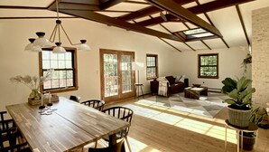 Un loft espacioso con techo alto, vigas de madera, un comedor con mesa y sillas largas, y una zona de estar acogedora con sofá y mesa de centro.