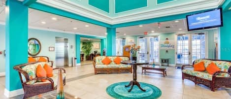 A spacious lobby with teal walls, wicker furniture, and a central round table.