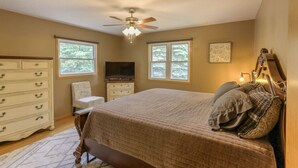 A bedroom with a bed, dresser, chair, television, windows, and a ceiling fan.