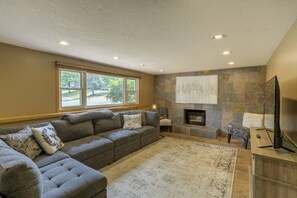 A living room with a sectional sofa, a fireplace, a television, and a large window.