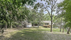 A backyard with a wooden deck, a small shed, and a hammock.