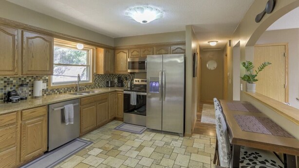 A kitchen with wooden cabinets, a stainless steel refrigerator, a dishwasher, and a window.