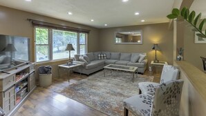 A living room with a sectional sofa, a flat-screen TV, a coffee table, and a patterned rug.