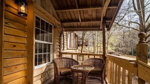 A wooden porch with wicker furniture and a window overlooking a forested area. - Hike the Holler - Stay & Explore (Cosby)