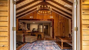 A log cabin interior with a high ceiling, wooden walls, a chandelier, a sofa, a dining table, and a kitchen area. - Hike the Holler - Stay & Explore (Cosby)