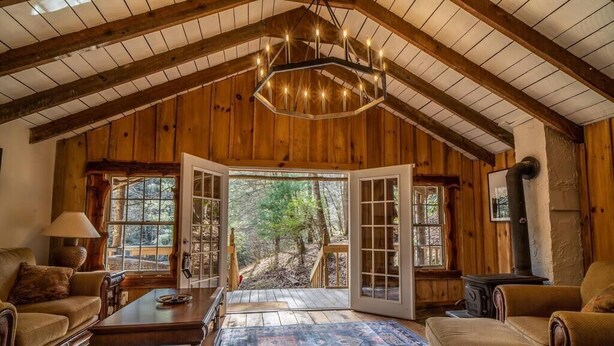 A cozy log cabin interior with a large open door leading to a deck, wooden furniture, and a fireplace. - Hike the Holler - Stay & Explore (Cosby)