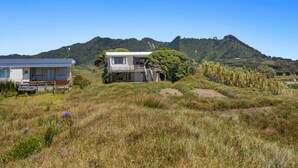 Una casa con un balcón y una pequeña escalera que lleva a un porche, rodeada de campos verdes y una colina al fondo.