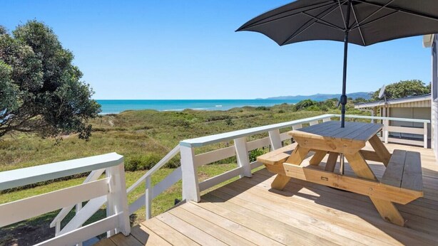 Una terraza de madera con mesa de picnic y sombrilla, con vistas al paisaje costero.