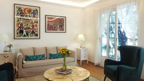 Una sala de estar con un sofá, una mesa de centro con un libro y un jarrón, un sillón verde y dos cuadros colgados en la pared.