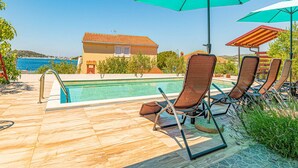 Ein Poolbereich mit Pool, Liegestühlen und Sonnenschirmen.