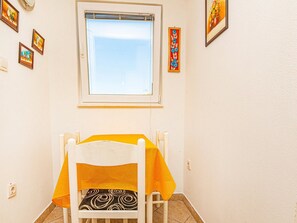 A small dining area with a white chair and table, a window above, and a few framed pictures on the walls. - Holiday Home Happy Holiday (Rogoznica)
