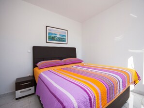 A bedroom with a bed, a nightstand, a framed picture on the wall, and a window.