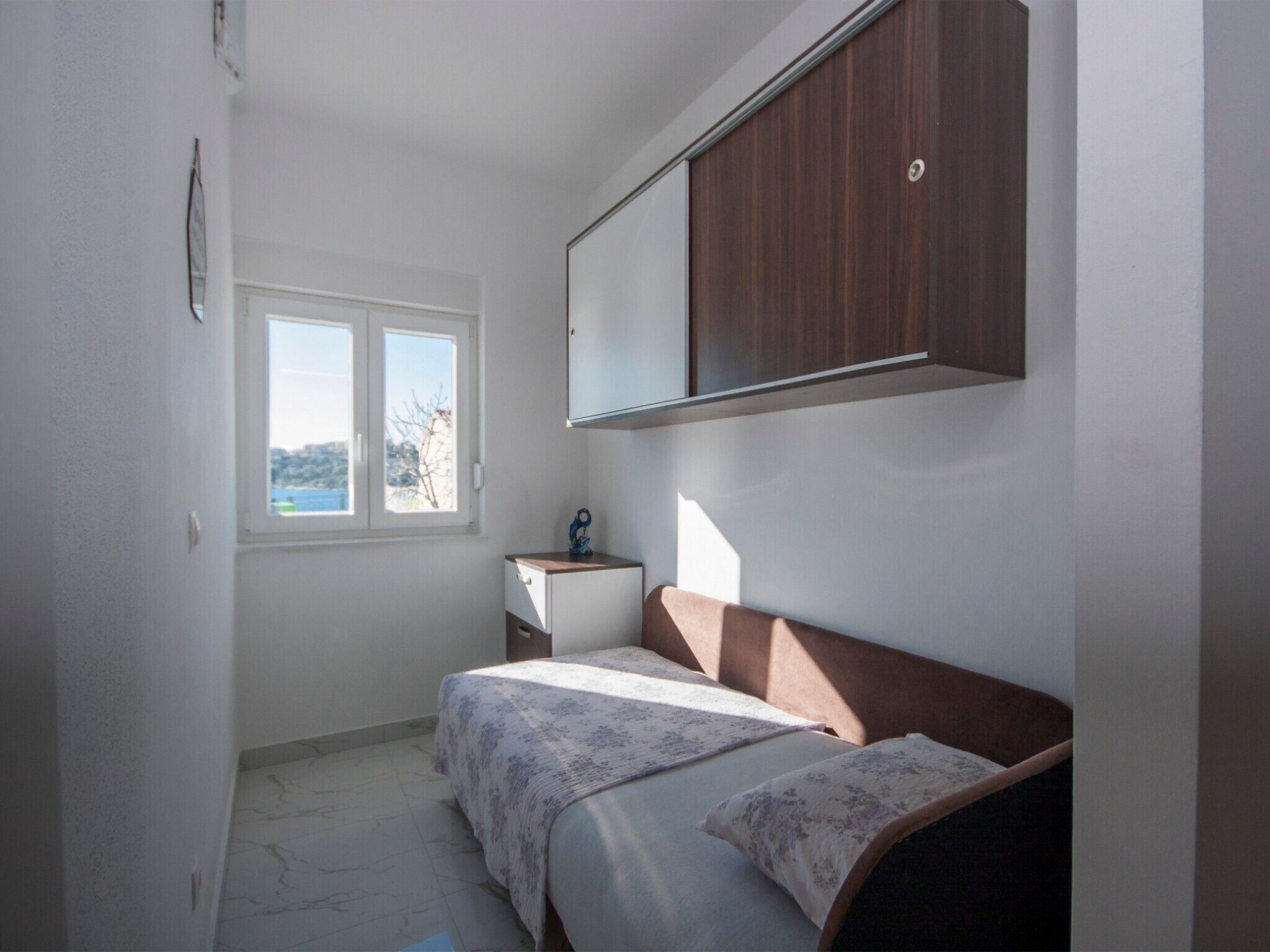 Quarto com cama, mesa de cabeceira, guarda-roupa e janela com vista.