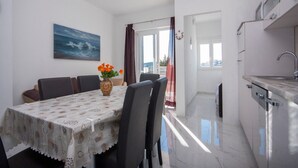 A dining area with a table set for four, a vase with flowers, and a painting of the sea on the wall. - Apartments Happy Holiday - Two Bedroom Apartment with Terrace (Rogoznica)
