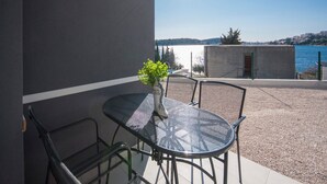 A balcony with a round metal table and chairs, a potted plant, and a view of a body of water and distant buildings. - Apartments Happy Holiday - Two Bedroom Apartment with Terrace (Rogoznica)