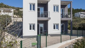 A modern two-story building with balconies, a fenced outdoor area, and a clear view of the surrounding landscape. - Apartments Happy Holiday - Two Bedroom Apartment with Terrace (Rogoznica)