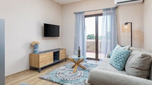 A modern living room with a flat-screen TV, a wooden cabinet, a glass coffee table, a sofa with patterned cushions, and a large sliding glass door leading to an outdoor area.