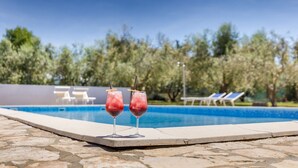 A poolside area with two drinks in glasses, a pool, and lounge chairs in the background. - Marceta Apartment 3 - Pool and Big Garden (Fažana)