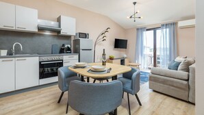 A modern kitchen with white cabinets, a dining table with four chairs, a TV, and a sofa in a living area. - Marceta Apartment 3 - Pool and Big Garden (Fažana)