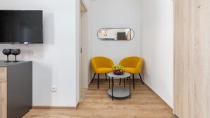 Ein modernes Zimmer mit einem Flachbildfernseher, zwei gelben Stühlen, einem kleinen runden Tisch mit Obst und einem Spiegel an der Wand.