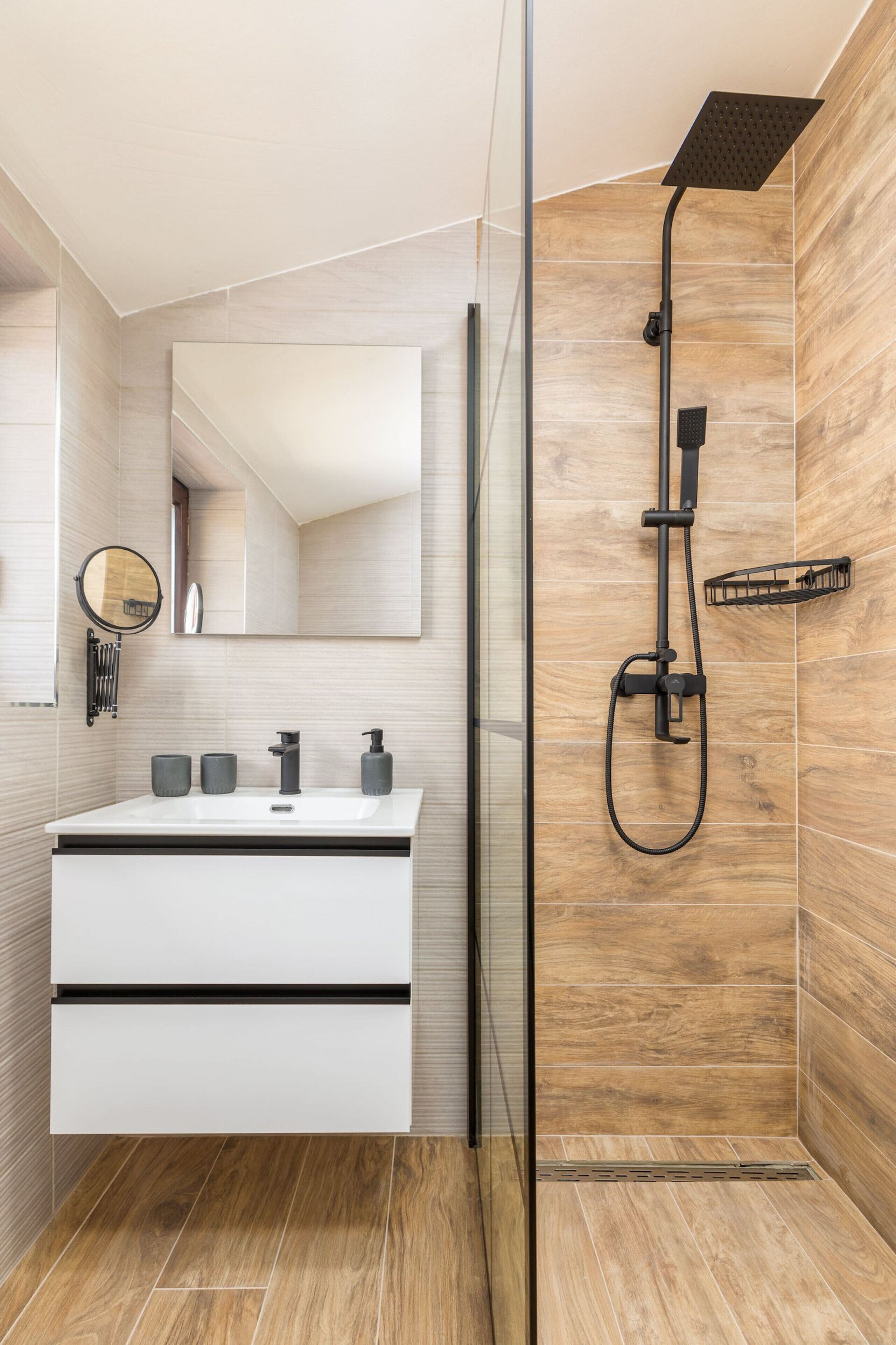 Un baño moderno con cabina de ducha de vidrio, un tocador blanco con pomos negros y un espejo grande sobre el lavabo.