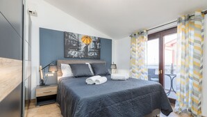 Ein modernes Schlafzimmer mit einem großen Bett, Nachttischen, einer Wandlampe und Blick ins Freie durch eine Schiebetür.