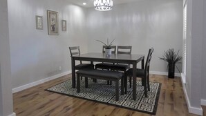 Un coin repas comprenant une table rectangulaire, six chaises, un tapis à motifs et un luminaire suspendu.