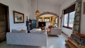 A living room with a sofa, armchairs, a television, and a stone archway. - Casa Coene, a charming, fully equipped Spanish house (Pals)