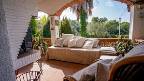 A cozy outdoor seating area with a sofa and chairs, a brick fireplace, and a view of lush greenery. - Casa Coene, a charming, fully equipped Spanish house (Pals)