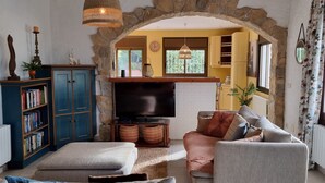 A cozy living room with a stone archway, a television, a bookshelf, and a comfortable sofa. - Casa Coene, a charming, fully equipped Spanish house (Pals)