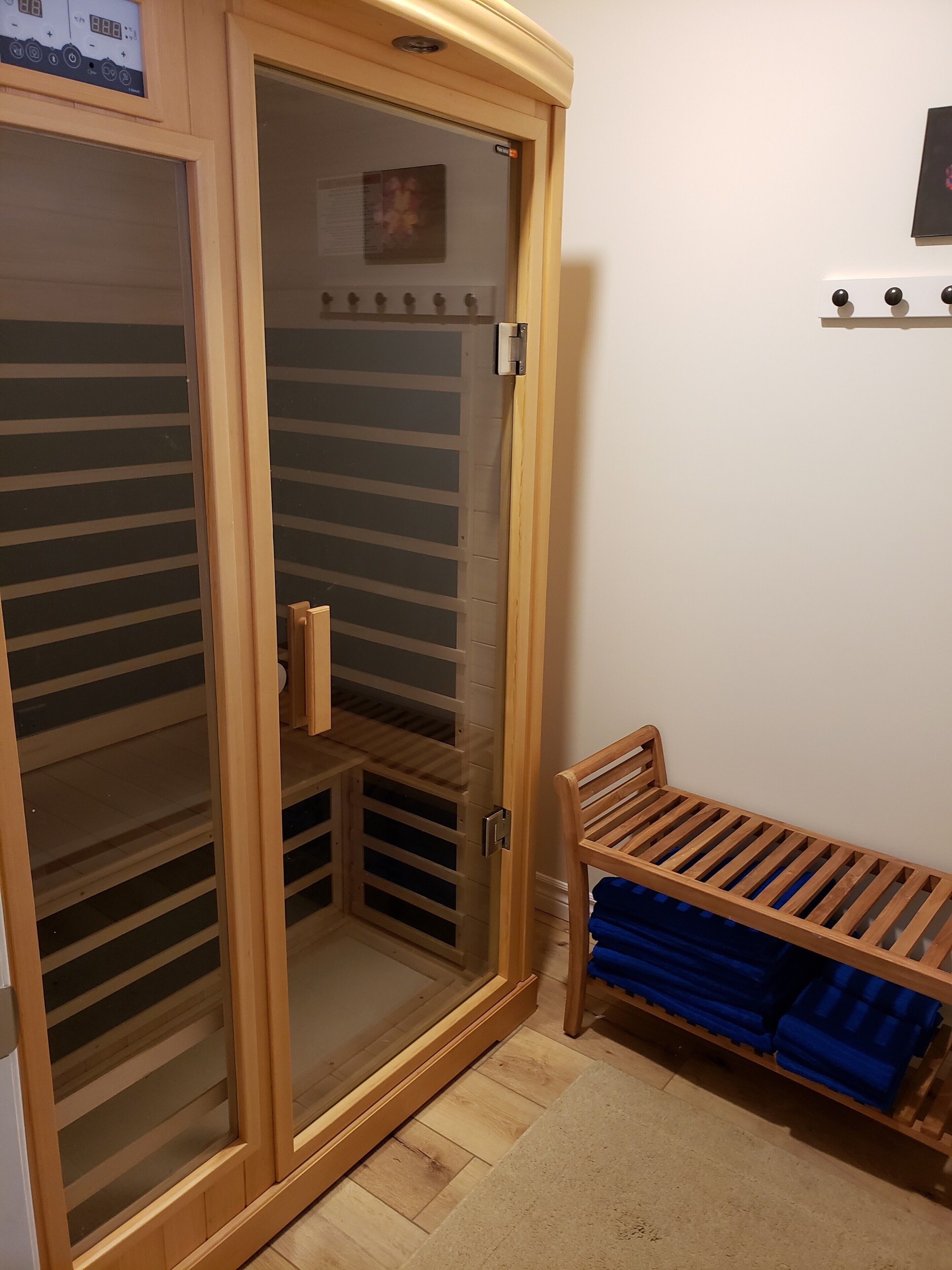 Une armoire en bois dotée d’une porte coulissante en verre, un banc avec des coussins bleus et une petite étagère sur laquelle est posé un cadre photo.