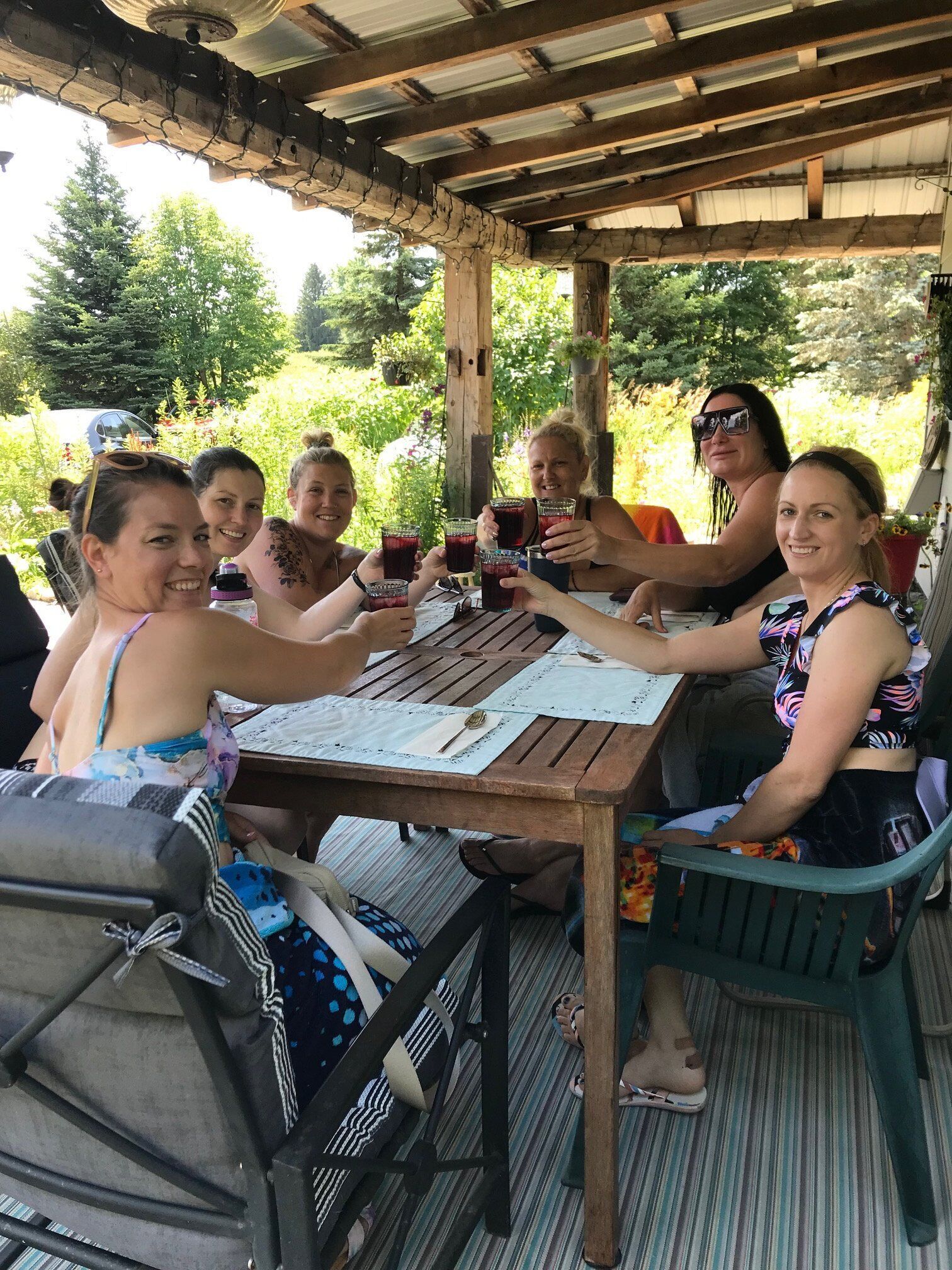 A group of people seated at a wooden table outdoors, with a pergola overhead.