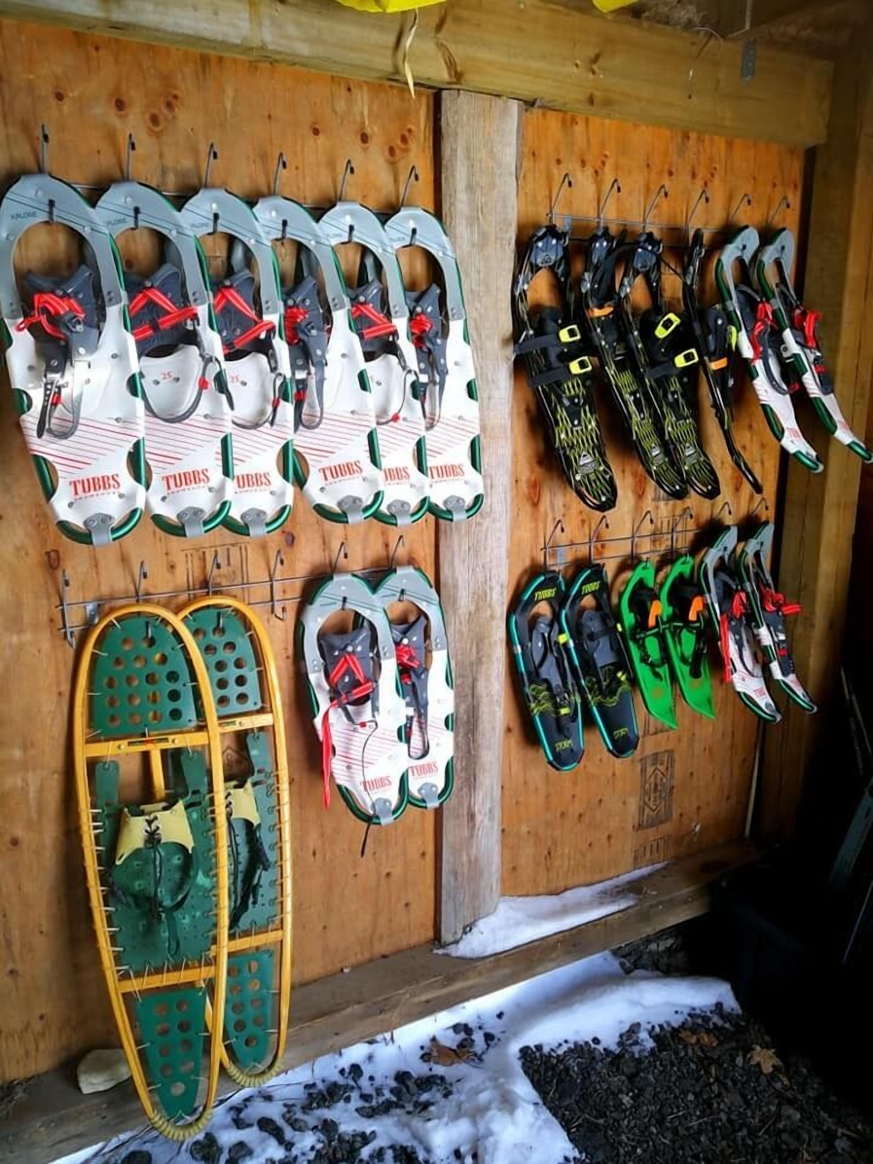 A wall with various snowshoes and snowboards hanging on hooks.