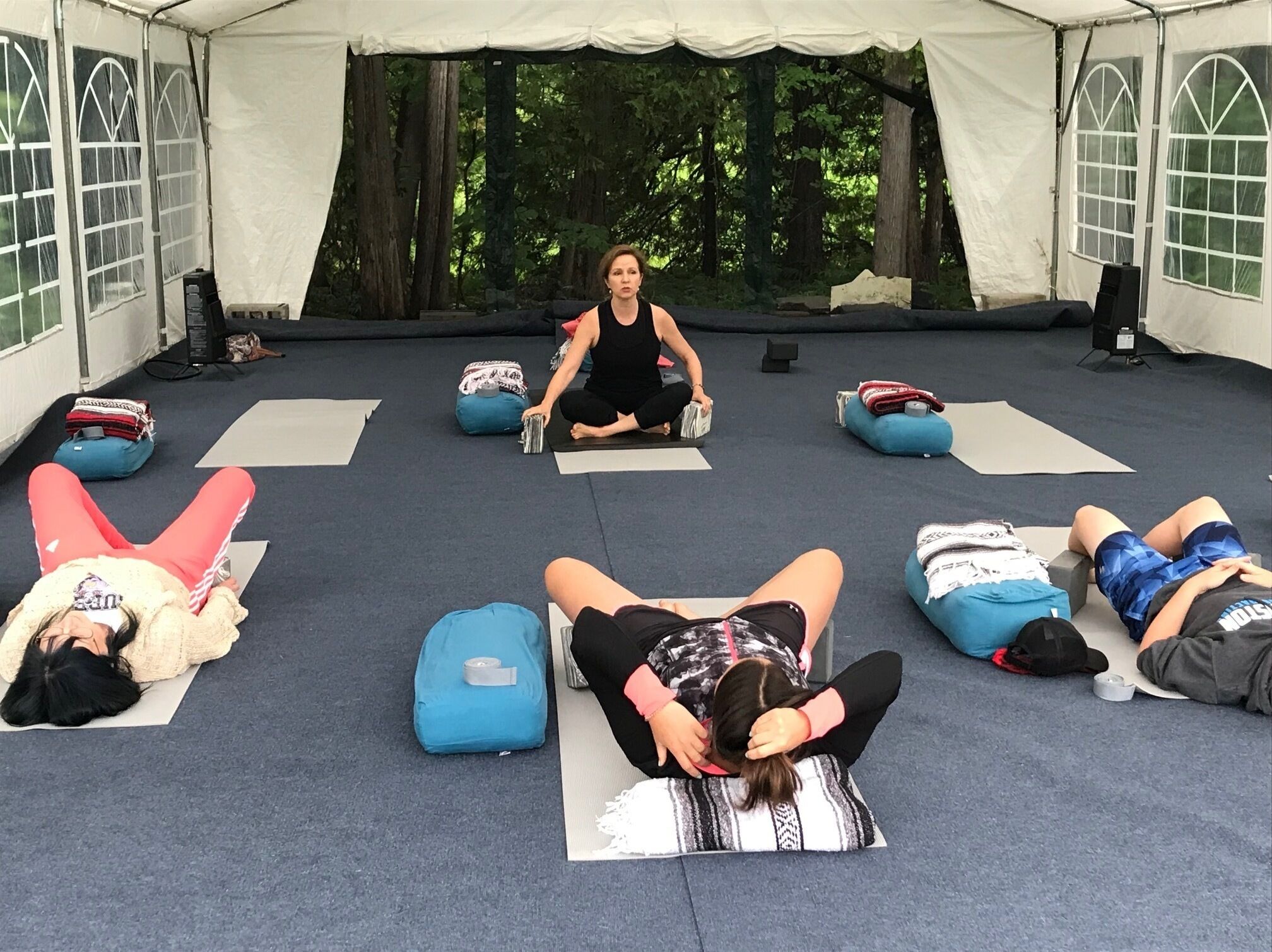 A group of people in a tented area, engaged in a yoga or stretching session.