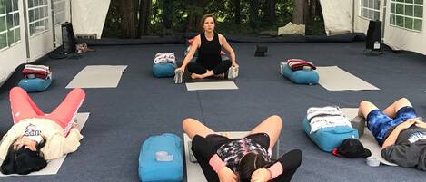 A group of people in a tented area, engaged in a yoga or stretching session.