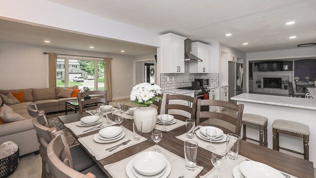 A modern kitchen with white cabinets, a central island, and a dining area with a wooden table set for four. - Family Retreat with Hot Tub & EV (Avon Lake)