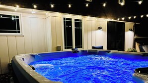 A hot tub with a blue light, surrounded by a white fence, and string lights above. - Family Retreat with Hot Tub & EV (Avon Lake)