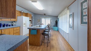 A kitchen with wooden cabinets, a refrigerator, a sink, and a bar stool.