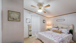 A bedroom with a bed, a ceiling fan, a nightstand, a lamp, a framed picture, and a decorative plant.