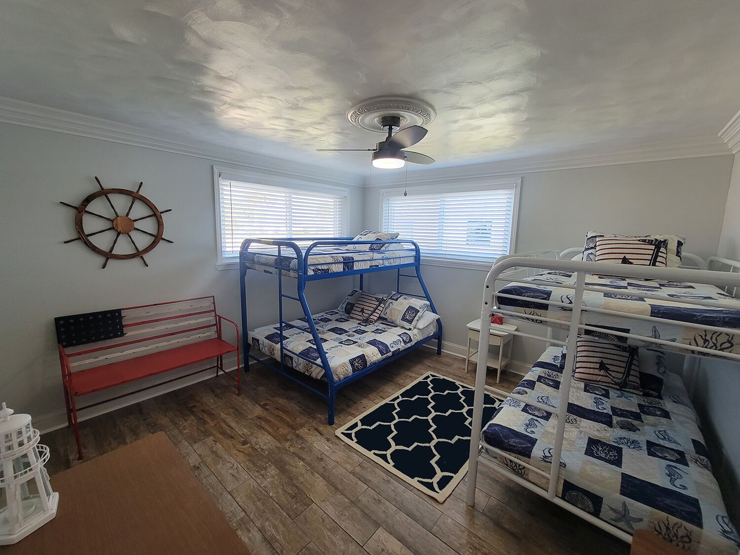 Een kamer met stapelbedden, een plafondventilator, een decoratie in de vorm van een schipsschroef en een raam met jaloezieën.