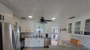 Eine moderne Küche mit weißen Schränken, einem Edelstahl-Kühlschrank, Granit Arbeitsplatten und einem Deckenventilator.