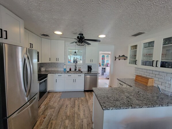 A modern kitchen with white cabinets, a stainless steel refrigerator, granite countertops, and a ceiling fan.