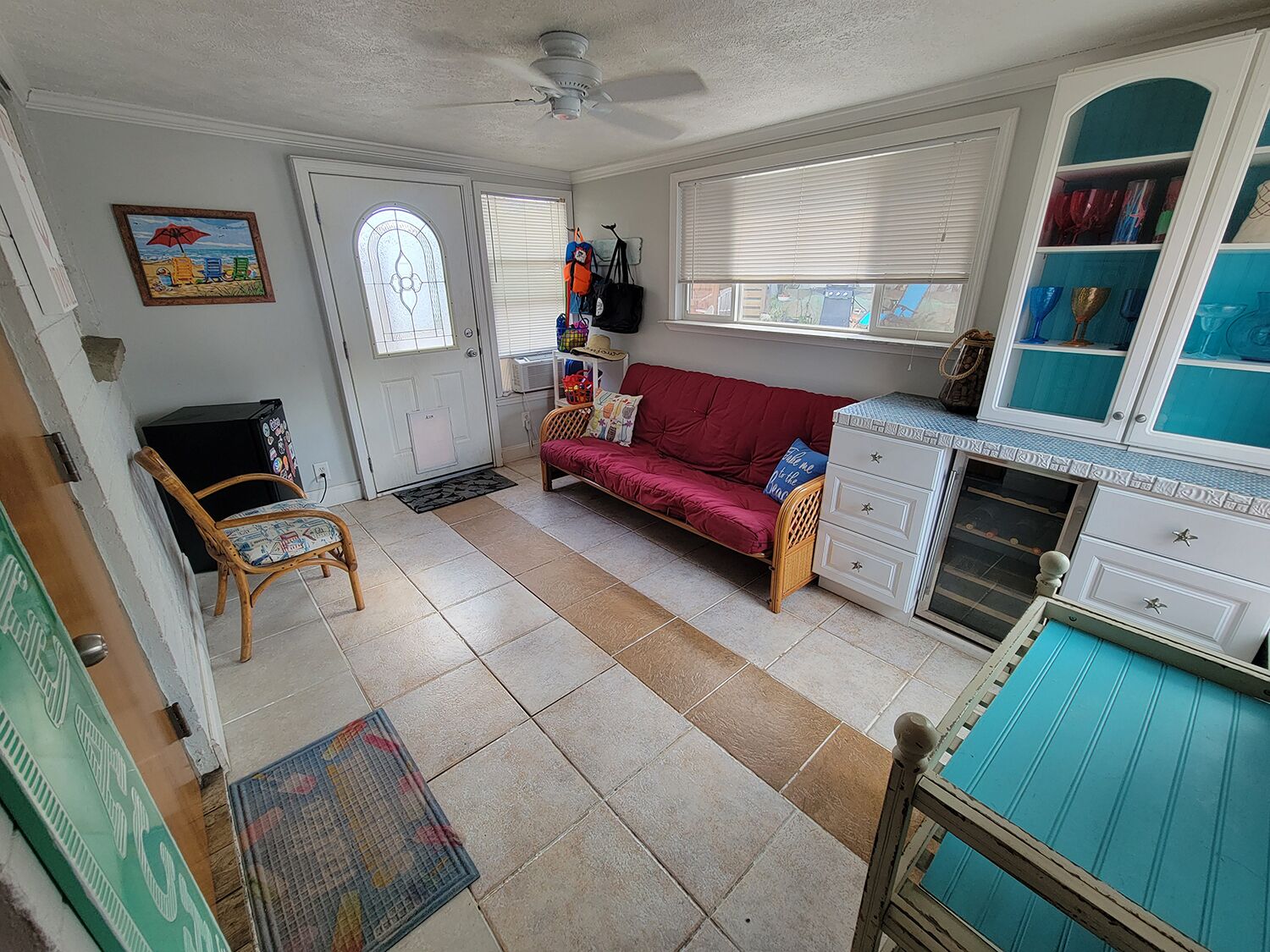 A living room with a red sofa, a wicker chair, a ceiling fan, and a window with blinds.